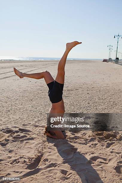 mann performing kopfstand am strand - den kopf in den sand stecken stock-fotos und bilder