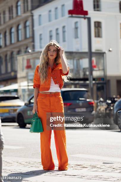 Emili Sindlev wearing orange wide pants, matching cropped short sleeves jacket, white top, green shoes and and green Hermes bag posing outside Saks...