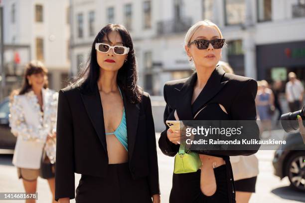 Pornwika Spiecker wearing black pants, blue bikini top, black crop jacket and white sunglasses and Justyna Czerniak wearing long pants with open...