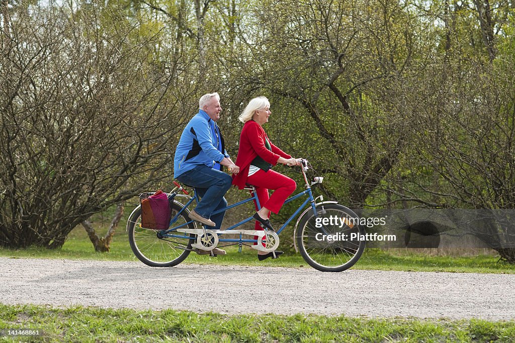 Senior couple riding tandem bike in park