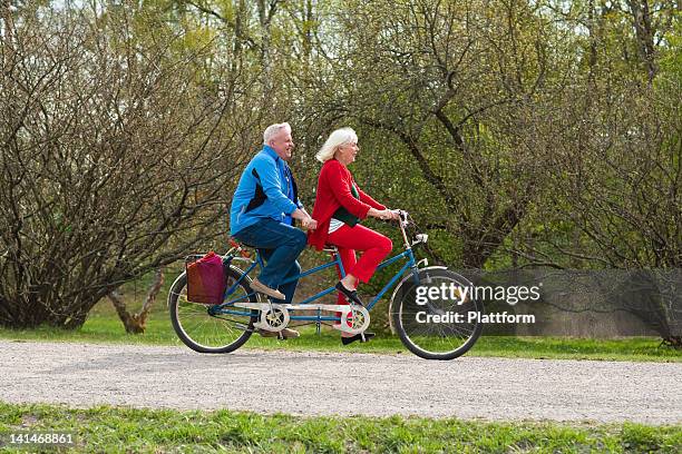 senior couple riding tandem bike in park - tandem stock pictures, royalty-free photos & images