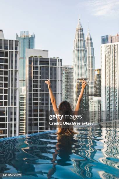 woman relaxing in luxury rooftop swimming pool with view of petronas twin towers in kuala lumpur. - kuala lumpur twin tower stock pictures, royalty-free photos & images