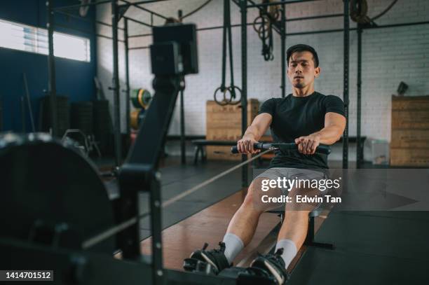 asian chinese gay man exercising on rowing machine in a gym - steel cable stock pictures, royalty-free photos & images