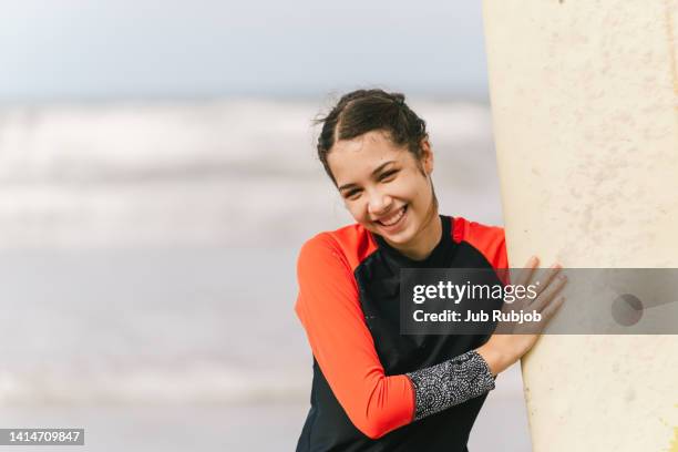 beautiful girl of asian ethnicity holding a surfer board with a smile - looking at camera australia stock-fotos und bilder