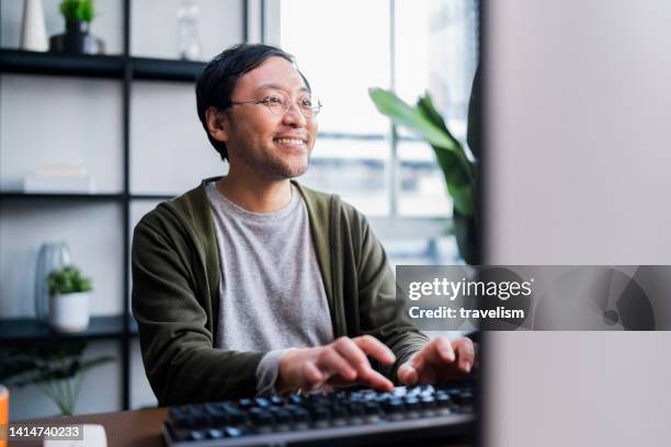 asian adult man working at home on holiday,home office: a happy young asian freelance creative man working in the comfort of his home, social distancing concept - personal computer 個照片及圖片檔