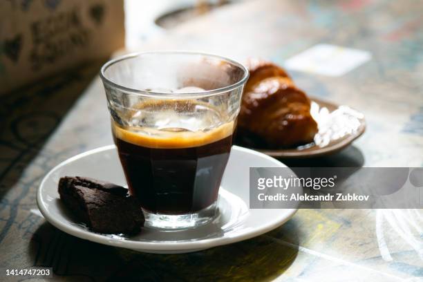 a mug of black coffee or americano, a croissant or a bun with raisins on the plane at the dining table in a cafeteria, restaurant, cafe or bakery. the concept of a coffee break, breakfast. fresh pastries. dependence on coffee and sweet food. - americano photos et images de collection