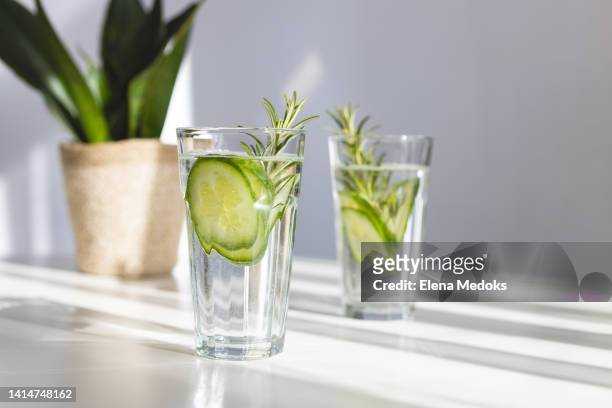 refreshing water with cucumber in glasses on the table against the window in the bright rays of the sun. summer cocktail with vegetables and fruits - gin stock-fotos und bilder