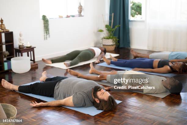 yoga class lying down in shavasana at end of class - body lying down stock pictures, royalty-free photos & images