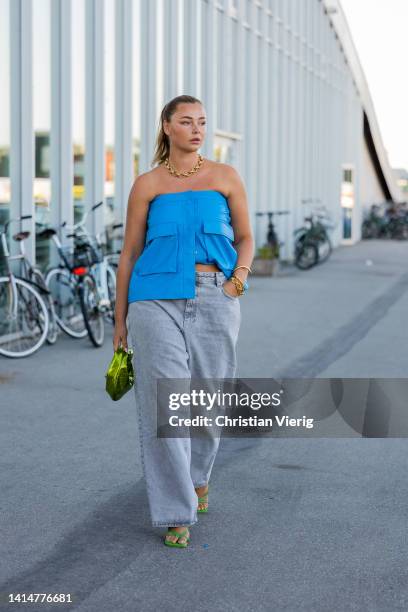 Guest is seen wearing blue off shoulder top, grey denim jeans, green bag outside Munthe during Copenhagen Fashion Week Spring/Summer 2023 on August...