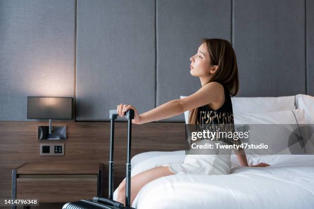 asian woman sitting on the bed in the hotel room after check in - jetlag stock-fotos und bilder