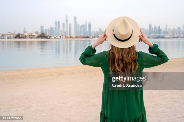 junge frau am strand mit blick auf die skyline von dubai - dubai travel stock-fotos und bilder