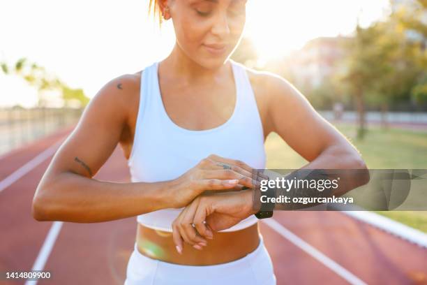 nahaufnahme einer jungen frau, die die smartwatch auf einer rennstrecke einstellt und überprüft. - frau uhr stock-fotos und bilder