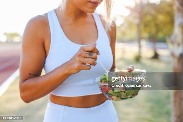 young woman eating a healthy salad after workout. fitness and healthy lifestyle concept. - custom fit stockfoto's en -beelden