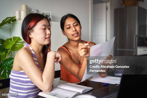 two classmates studying at home and one of them points out something on a sheet of paper to the other one - exactitud fotografías e imágenes de stock