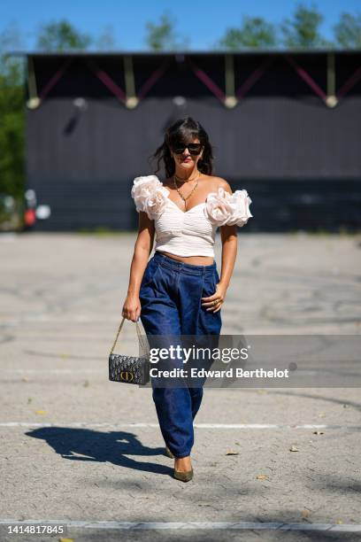 Gili Biegun wears black sunglasses, a gold double necklace from Hermes, a white matte ruffled / V-neck / embroidered large flower / cropped top, navy...