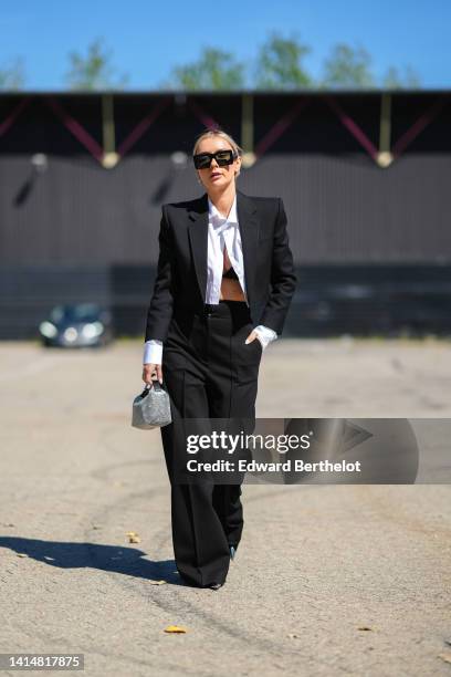 Jusytna Czerniak wears black square sunglasses, a black cropped / shoulder-pads blazer jacket, high waist black wide legs pants, a white cropped...