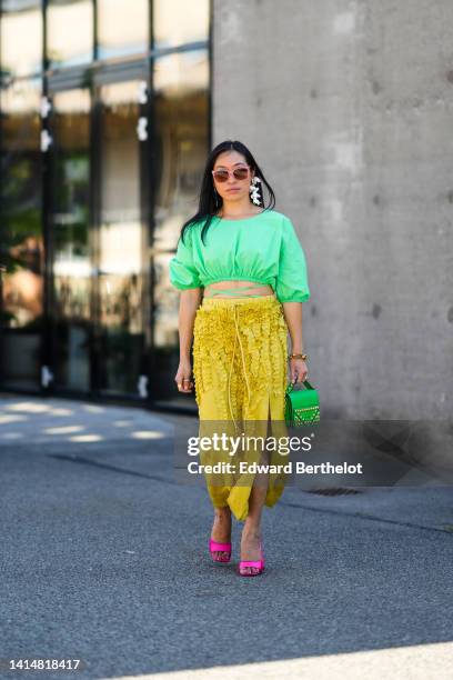 Miki Cheung wears pink sunglasses, silver pendant earrings, a green cropped / laces waist / puffy short sleeves top, a white flower pendant earring,...