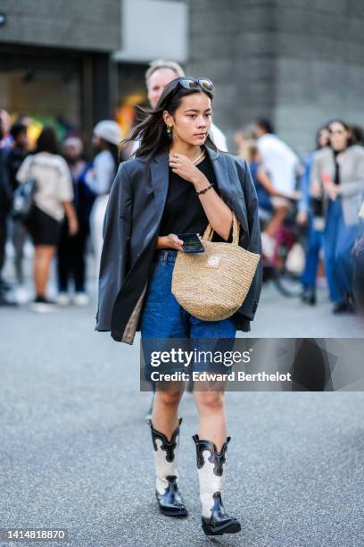 Guest wears sunglasses, fruit gold pendant earrings, a white pearls necklace, gold rings, a black t-shirt, a gray oversized blazer jacket, a beige...