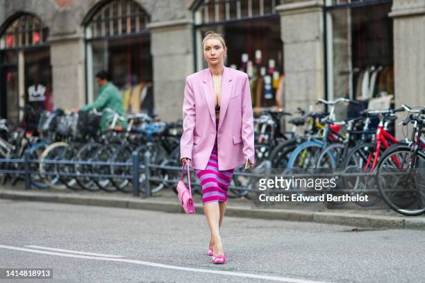 Justyna Czerniak wears silver earrings, a pale pink oversized blazer jacket, a black V-neck bra underwear, a pink shiny leather Baguette handbag from...