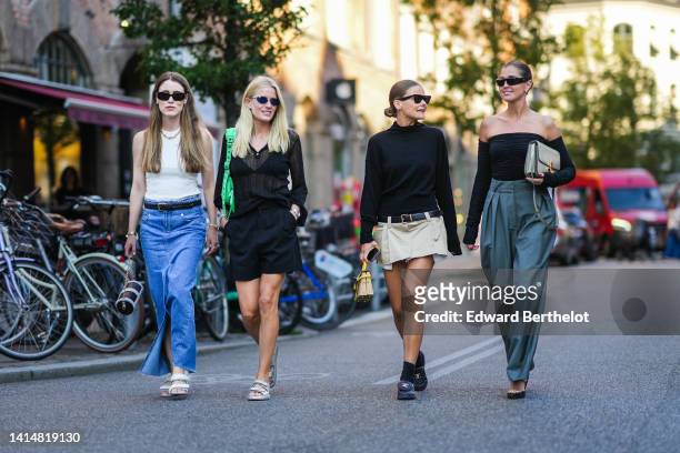 Annabel Rosendahl wears black sunglasses, earrings, a gold large chain necklace, a white ribbed halter-neck tank-top, a black braided shiny leather...