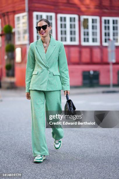 Guest wears black sunglasses, silver earrings, a silver chain pendant necklace, a white and green checkered print pattern blazer jacket, matching...