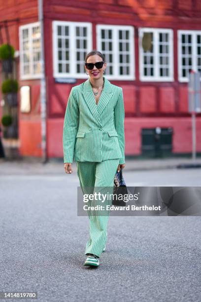 Guest wears black sunglasses, silver earrings, a silver chain pendant necklace, a white and green checkered print pattern blazer jacket, matching...