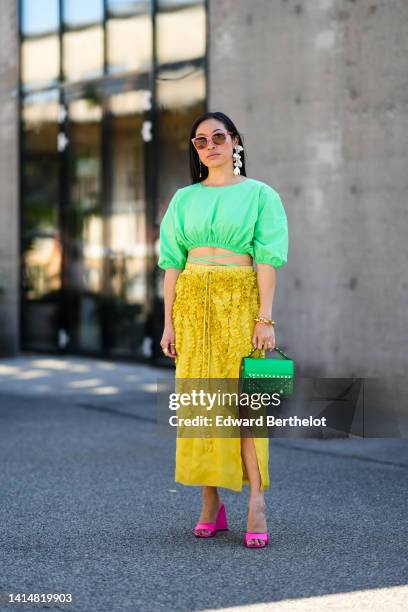 Miki Cheung wears pink sunglasses, silver pendant earrings, a green cropped / laces waist / puffy short sleeves top, a white flower pendant earring,...