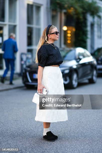 Guest wears a black checkered embossed pattern headband, black sunglasses, gold earrings, gold chain necklaces, a black embossed checkered pattern /...