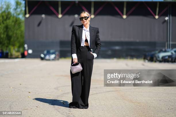 Jusytna Czerniak wears black square sunglasses, a black cropped / shoulder-pads blazer jacket, high waist black wide legs pants, a white cropped...