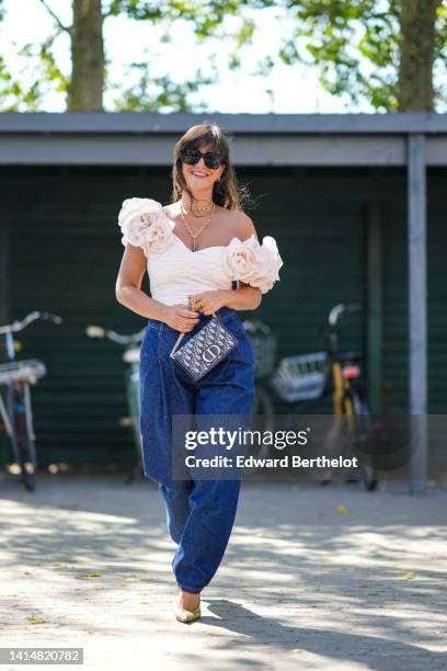 Gili Biegun wears black sunglasses, a gold double necklace from Hermes, a white matte ruffled / V-neck / embroidered large flower / cropped top, navy...