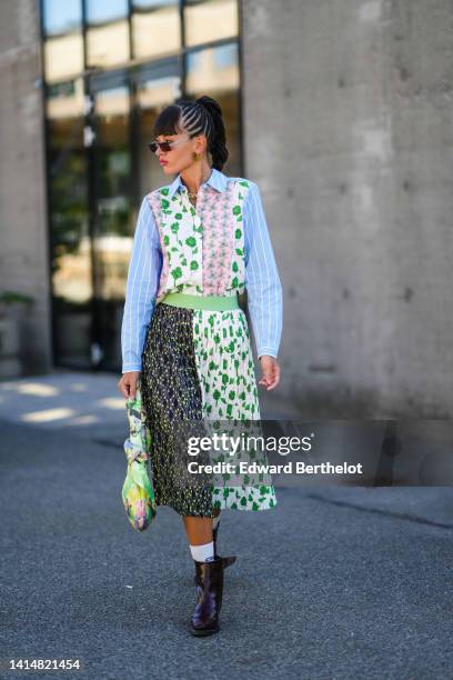 Katya Tolstova wears black square sunglasses, brown and green plastic earrings, a baby blue and white striped print pattern with white / green / pink...