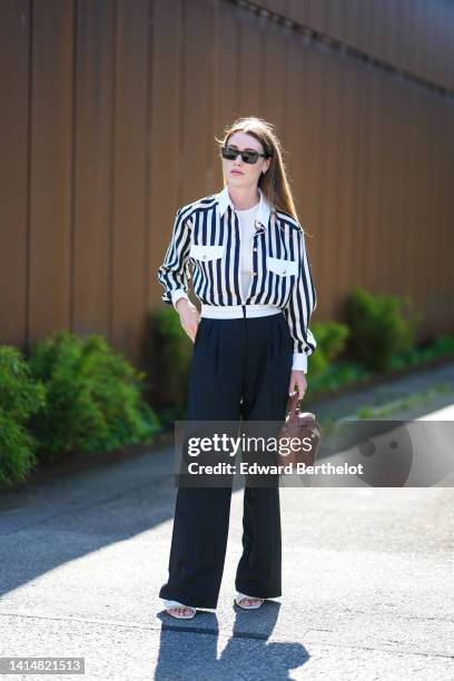 Annabel Rosendahl wears black square sunglasses, a white t-shirt, a black and white striped print pattern cropped shirt jacket, high waist navy blue...