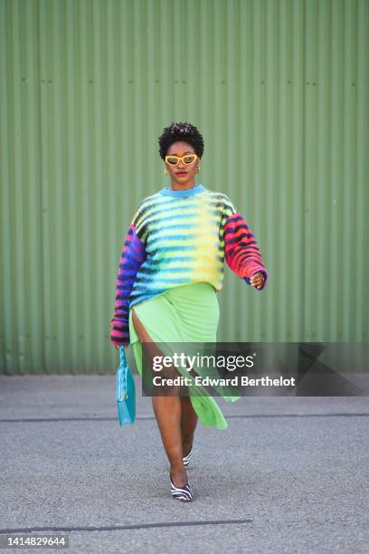 Guest wears yellow sunglasses, gold earrings, gold chain pendants necklaces, a black with multicolored print pattern wool pullover, a green ribbed...