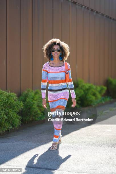 Guest wears black sunglasses, blue pearls pendant earrings, a gold chain and multicolored pearls necklace, a pale purple / blue / orange striped...