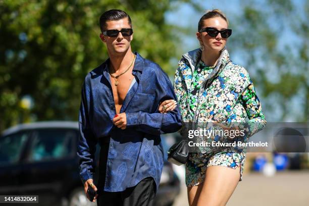 Guest wears black sunglasses from Prada, a gold large chain necklace from Prada, a gold long pendant necklace, a navy blue print pattern silk shirt,...