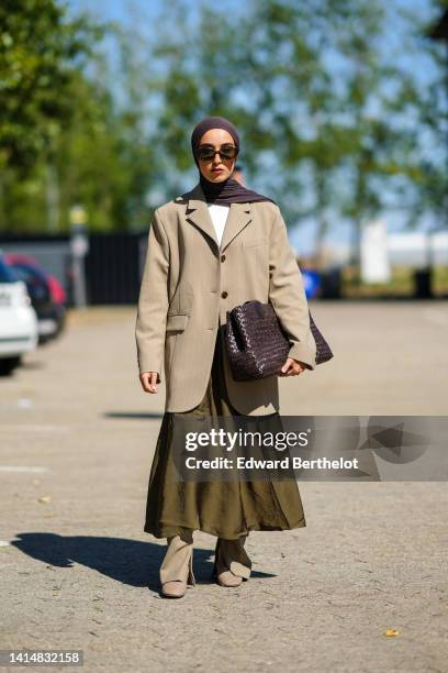 Guest wears a dark brown scarf, dark brown sunglasses, a white t-shirt, a beige oversized blazer jacket, a khaki linen long skirt, a dark brown shiny...