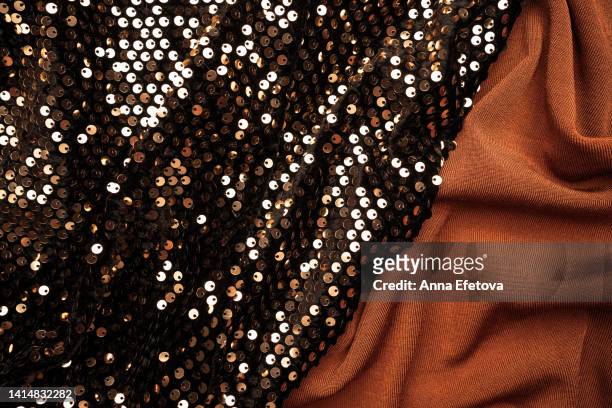 festive background made with different fabrics. many golden sequins on black velvet near brown textile. close-up - jersey top stockfoto's en -beelden