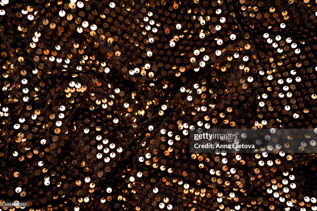 Many golden sequins on black velvet. Fragment of beautiful festive dress. Close-up