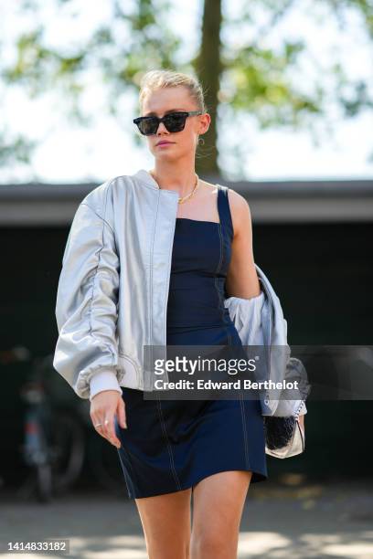 Guest wears black sunglasses, a silver and diamonds necklace, a black sunglasses, a black square-neck / tank-top short dress, a silver shiny leather...