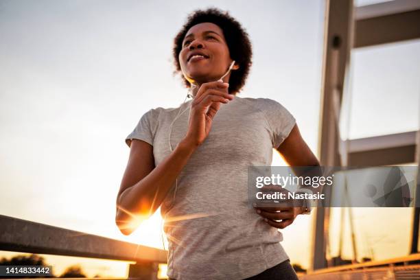 jogging across the bridge at sunset - woman headphones sport smile iphone stock pictures, royalty-free photos & images