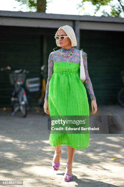 Guest wears white cat eyes sunglasses, a white pearls with multicolored pendant necklaces, a blue / purple / orange flower print pattern high neck /...