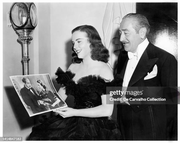 Canadian Actress and Singer Deanna Durbin and Actor Adolphe Menjou are on the set of 'I’ll Be Yours' looking at a picture of themselves together...