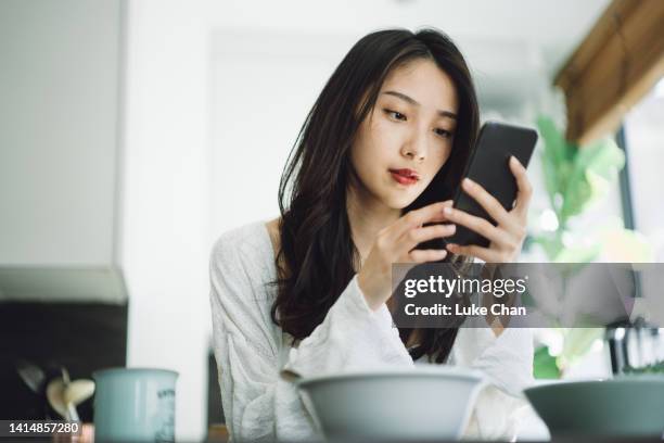 young asian woman using smartphone at home - cell phone confused stockfoto's en -beelden