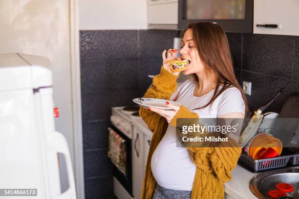 pregnant woman eating a sandwich at home - pregnancy healthy eating stock pictures, royalty-free photos & images