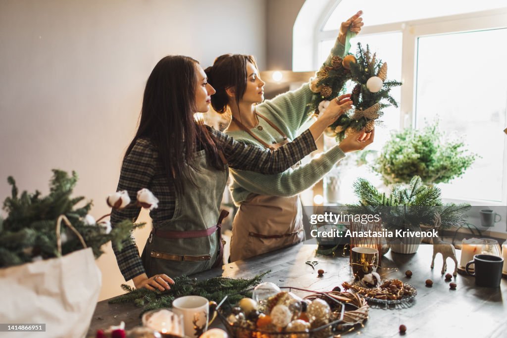 Two women making Christmas wreath using fresh pine branches and festive decorations.