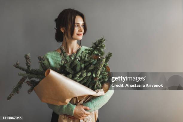 woman holding craft bag with christmas tree branches against grey wall. - christmas garland stock pictures, royalty-free photos & images