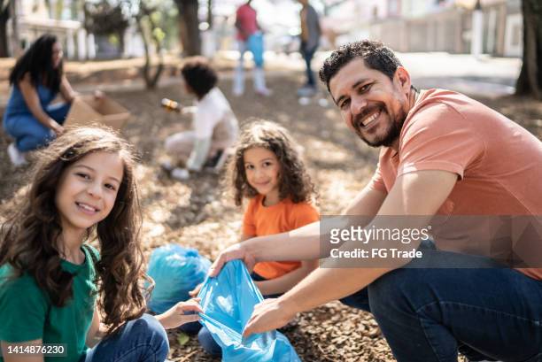 portrait of father and daughters picking up garbage at a public park - father and children volunteering imagens e fotografias de stock
