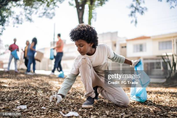 boy picking up garbage to clean a public park - picking up kids stock pictures, royalty-free photos & images