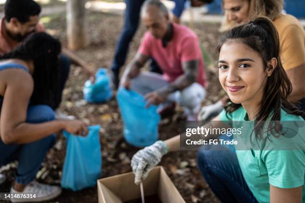 portrait of a young woman picking up garbage to clean a public park - social responsibility 個照片及圖片檔