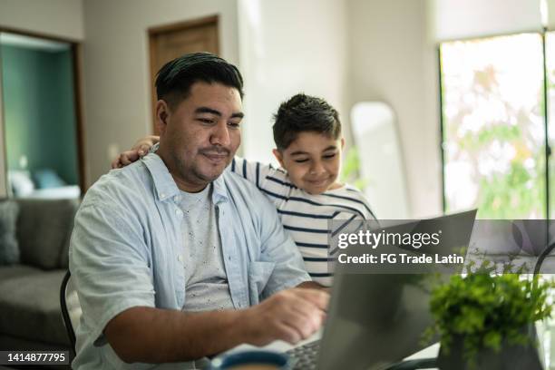 padre usando computadora portátil trabajando con el hijo en casa - padres-amos-de-casa fotografías e imágenes de stock